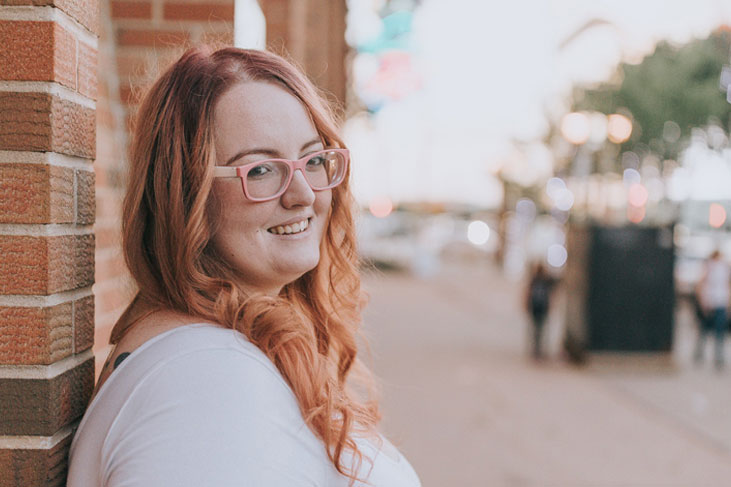 A woman leaning on a wall outside smiles at camera