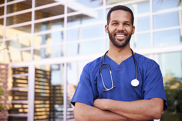 Man wearing scrubs smiling with arms crossed